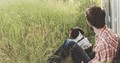 young man sitting with his dog in long grass against a wall